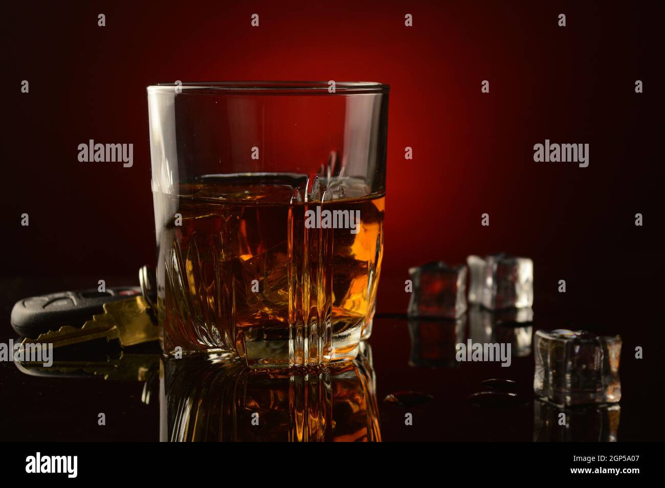 A concept image of drinking and driving utilizing a set of car keys next to a glass of whiskey over a dark reflective black and red background. Stock Photo