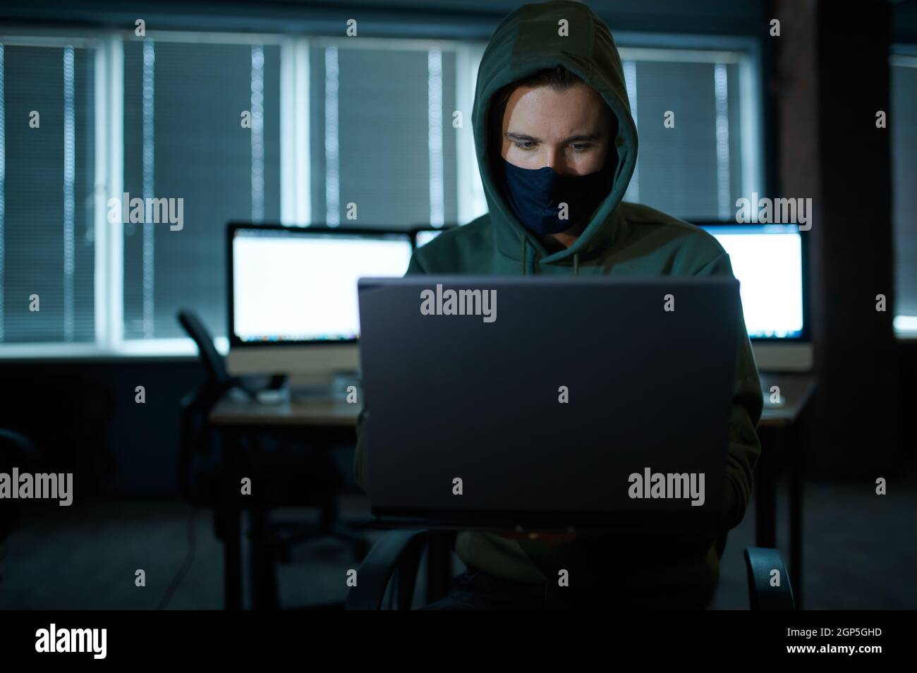 Male internet hacker in hood holds laptop, front view. Illegal web 