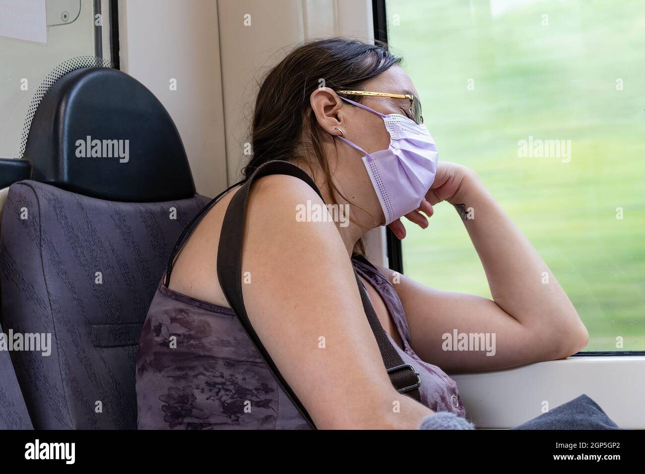 Barcelona, Spain - September 21, 2021: Exhausted woman take a nap on the train during her way to home. She is using a protective face mask due to coro Stock Photo