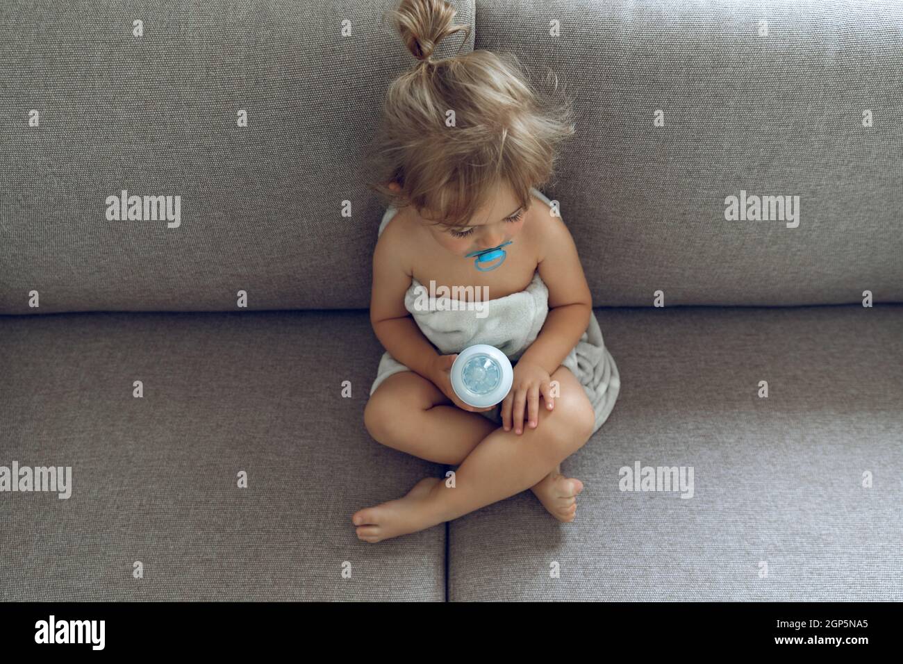 Cute Little Baby With Pleasure Spending Time at Home. Sitting on the Couch Preparing for a Meal. Baby Milk Formula. Healthy Organic Babies Nutrition. Stock Photo