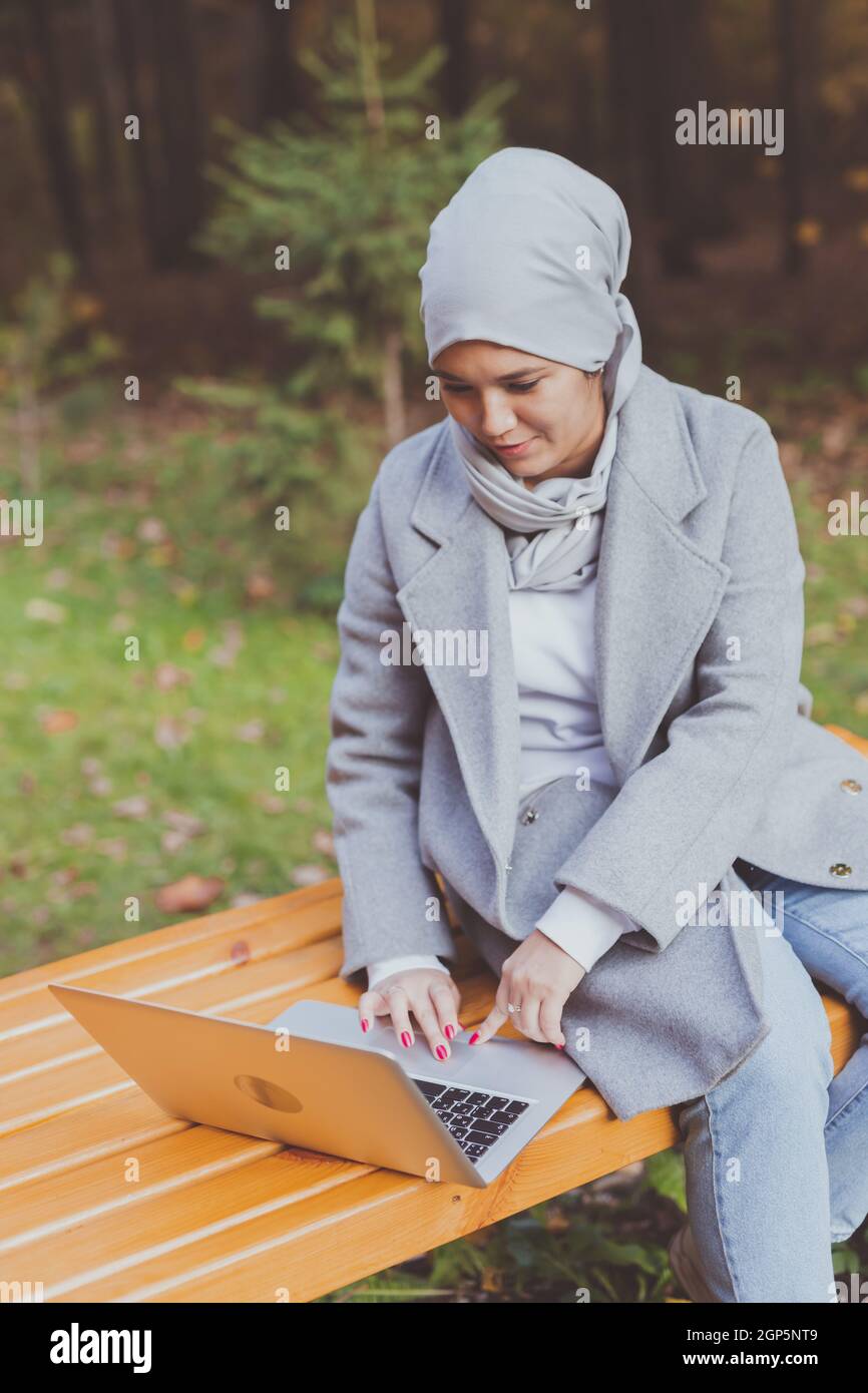 Young asian muslim woman using laptop at autumn park. Online education ...