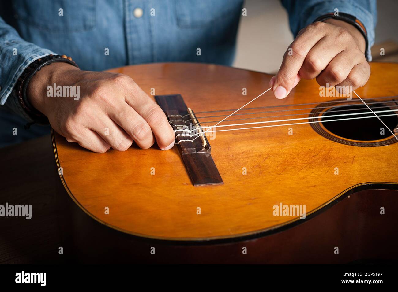 closeup man's hand changing strings on his old acoustic guitar Stock
