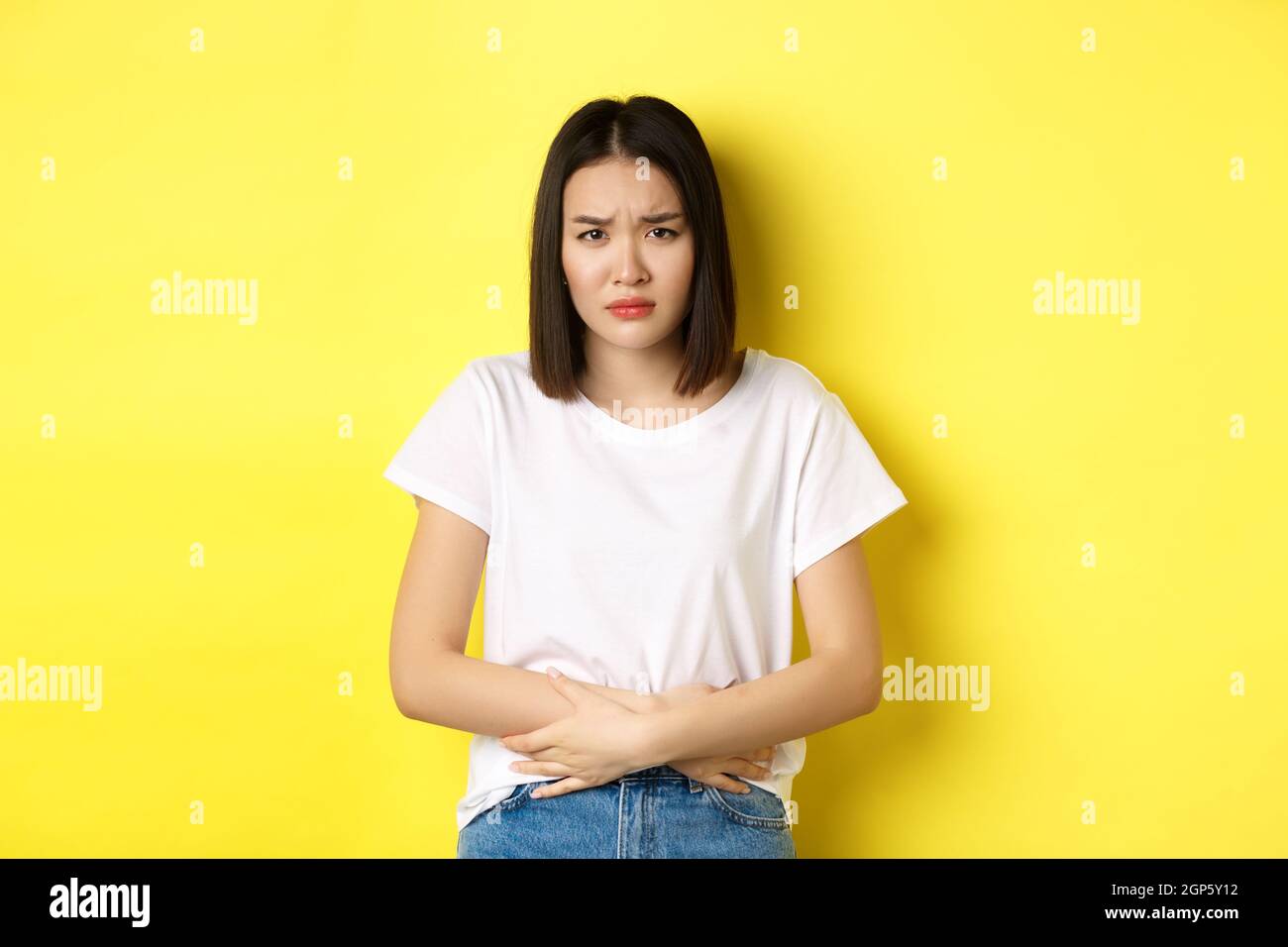 Image of asian woman feeling sick, having painful cramps, holding hands