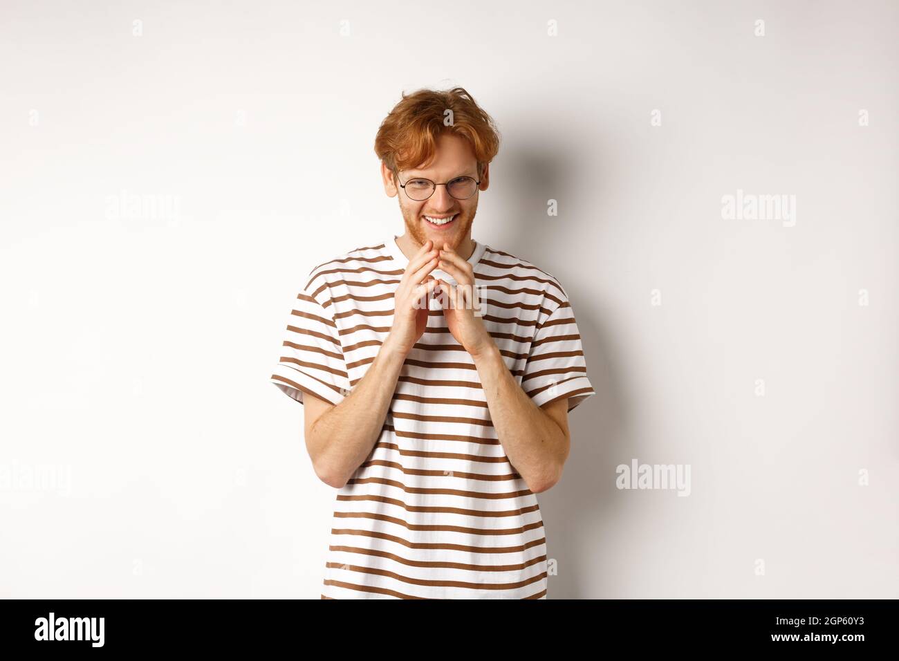 Portrait of redhead man looking like evil genius, steeple fingers and chuckling devious, scheming some plan, standing over white background. Stock Photo