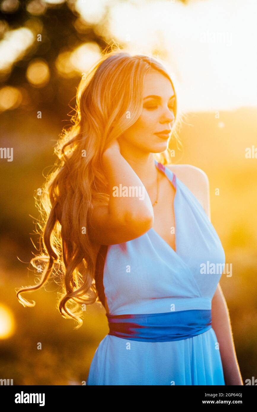 blonde with loose hair in a light blue dress in the light of sunset in  nature Stock Photo - Alamy