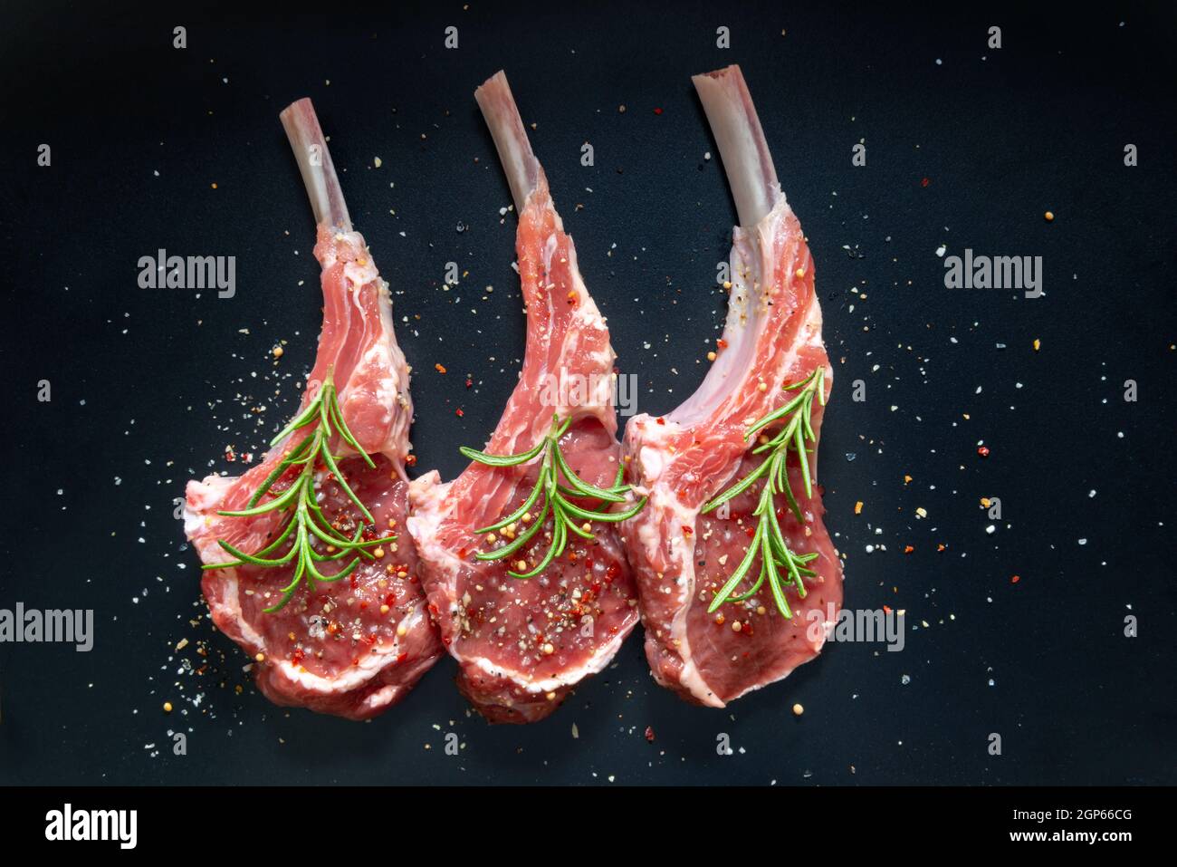 raw lamb saddle meat on bone with salt, pepper decorated rosemary top view on black background Stock Photo