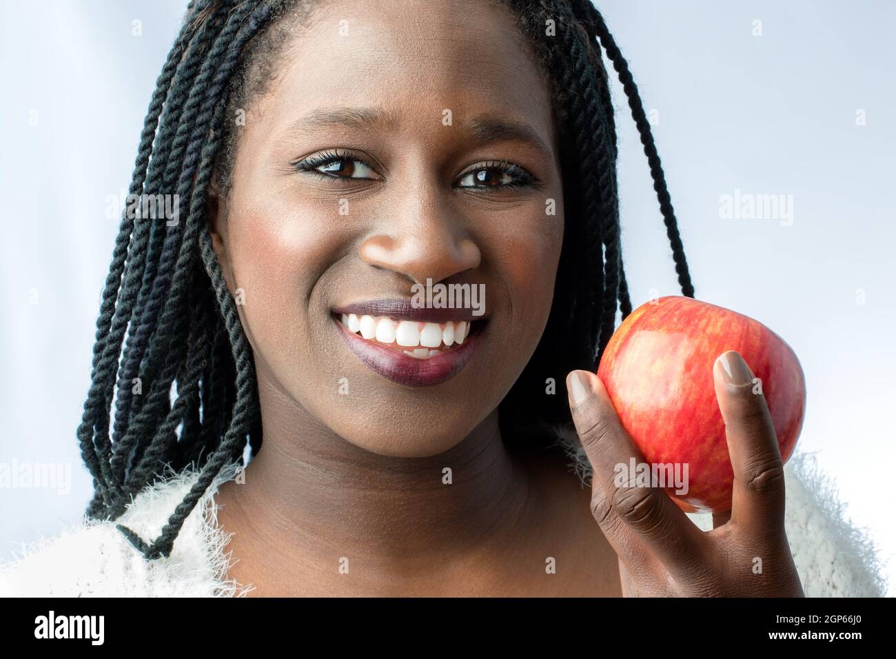 Macro close up of cute african teen with charming smile holding red apple.Isolated on light background. Stock Photo