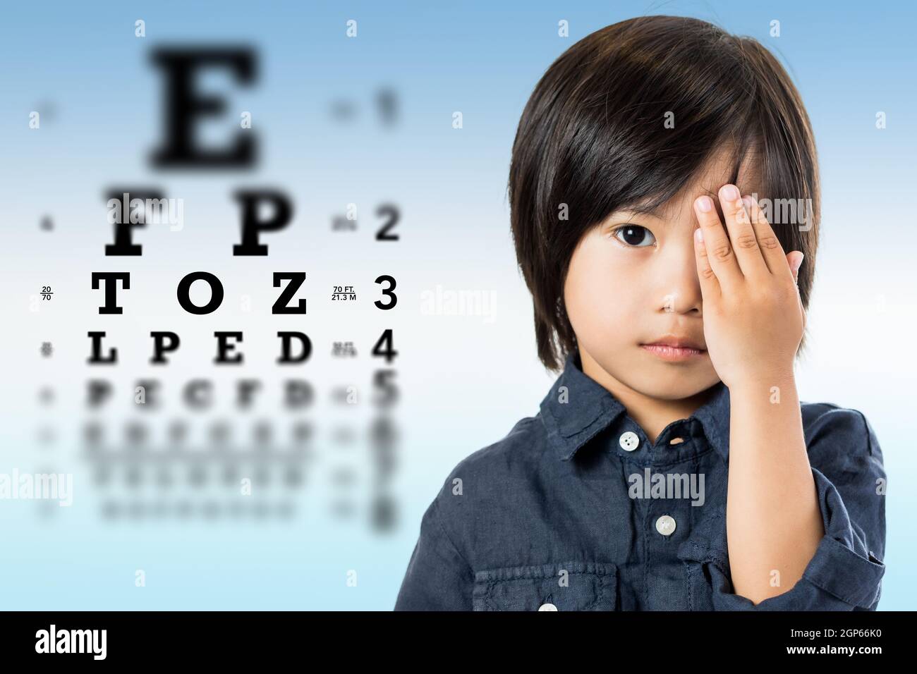 Close up portrait of handsome little asian boy testing eyesight.Kid closing one eye with hand against alphabetical out of focus eye test chart in back Stock Photo