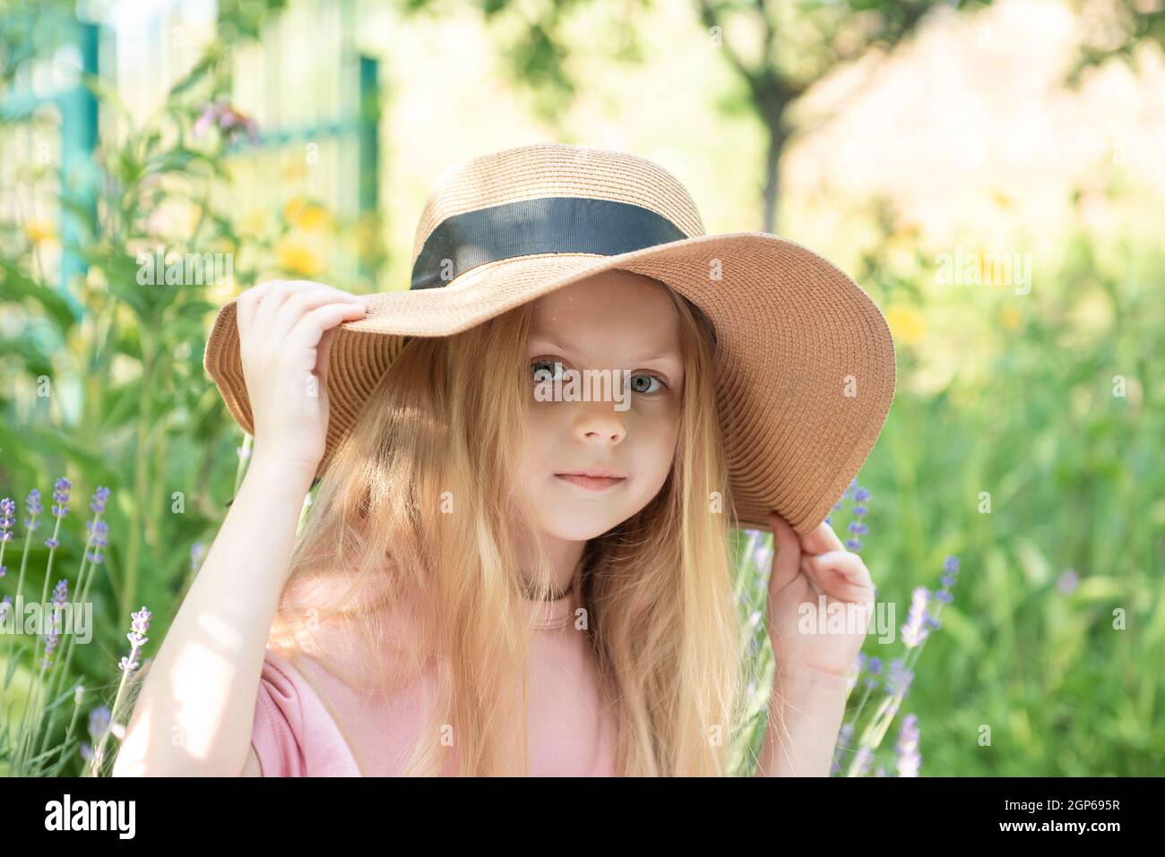 Little girl in a straw hat surrounded by lavender flowers. Portrait of ...
