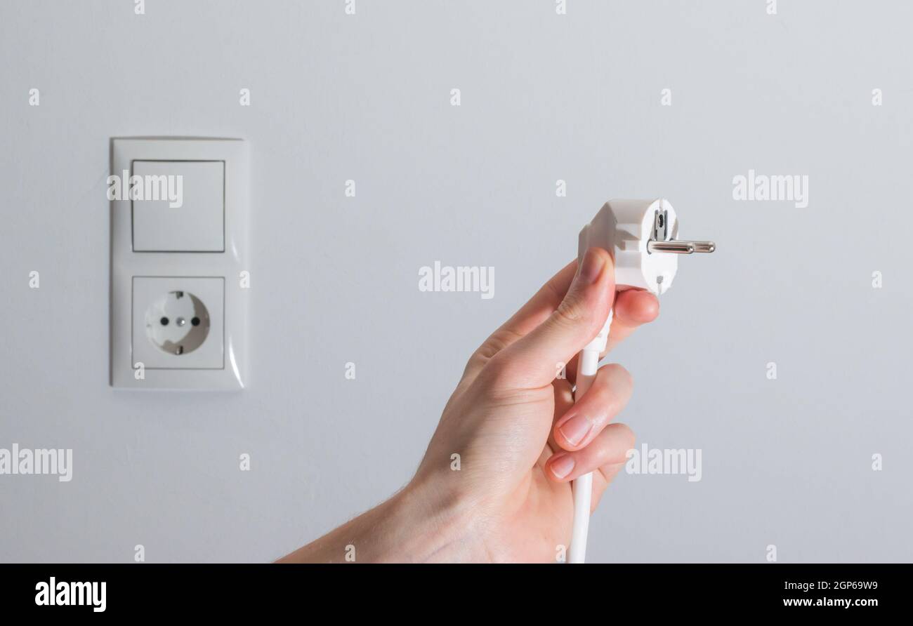 White plug with cable in males hand, ready to connect. Energy concept ...