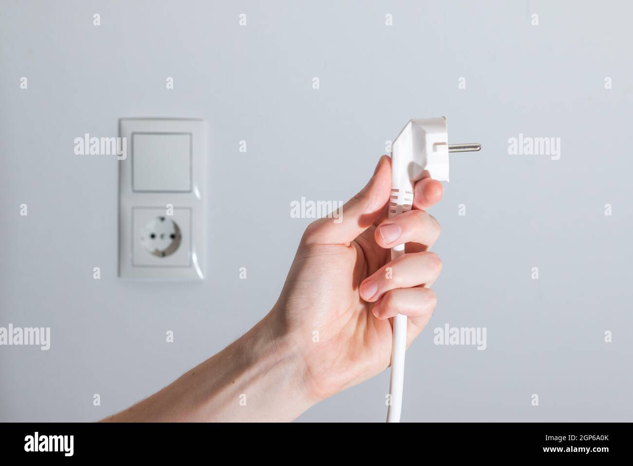White plug with cable in males hand, ready to connect. Energy concept ...