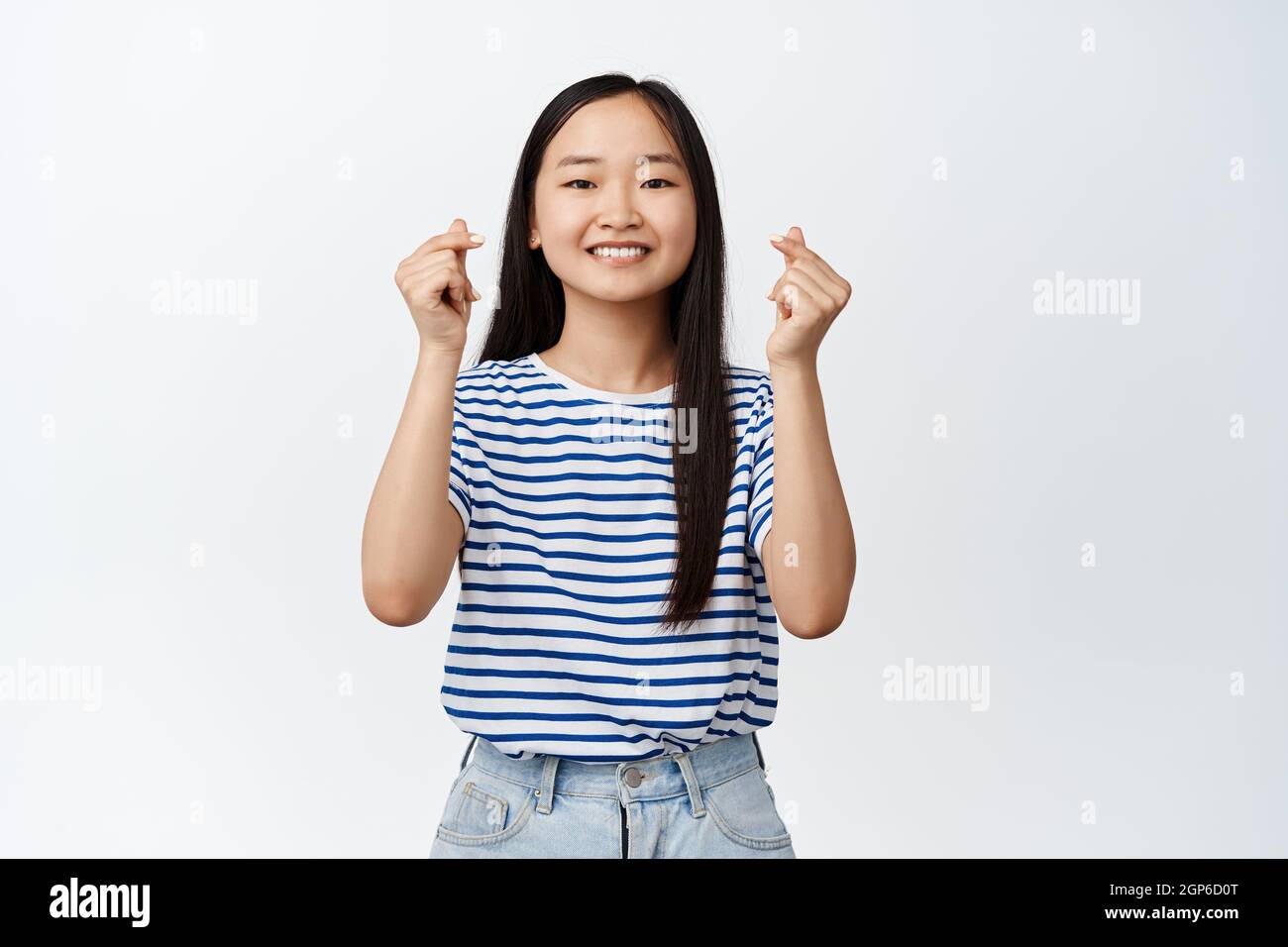 Cute korean girl shows finger hearts gesture and smiling, optimistic and  positive face expression, happy attitude, standing over white background  Stock Photo - Alamy