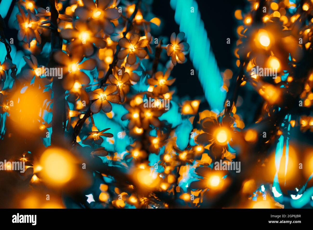 Garland on tree. Colorful light bulbs in the form of flowers. Bright festive lighting of the city. Illumination at night. Winter holiday. Concept of Christmas and New year. Stock Photo