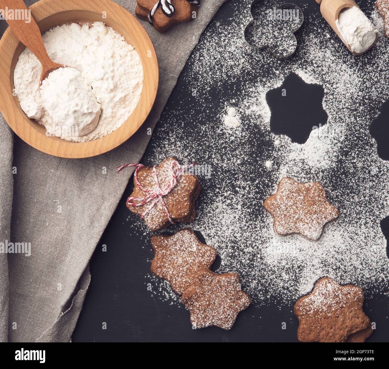 baked star-shaped gingerbread cookie sprinkled with powdered sugar on a black table and ingredients Stock Photo