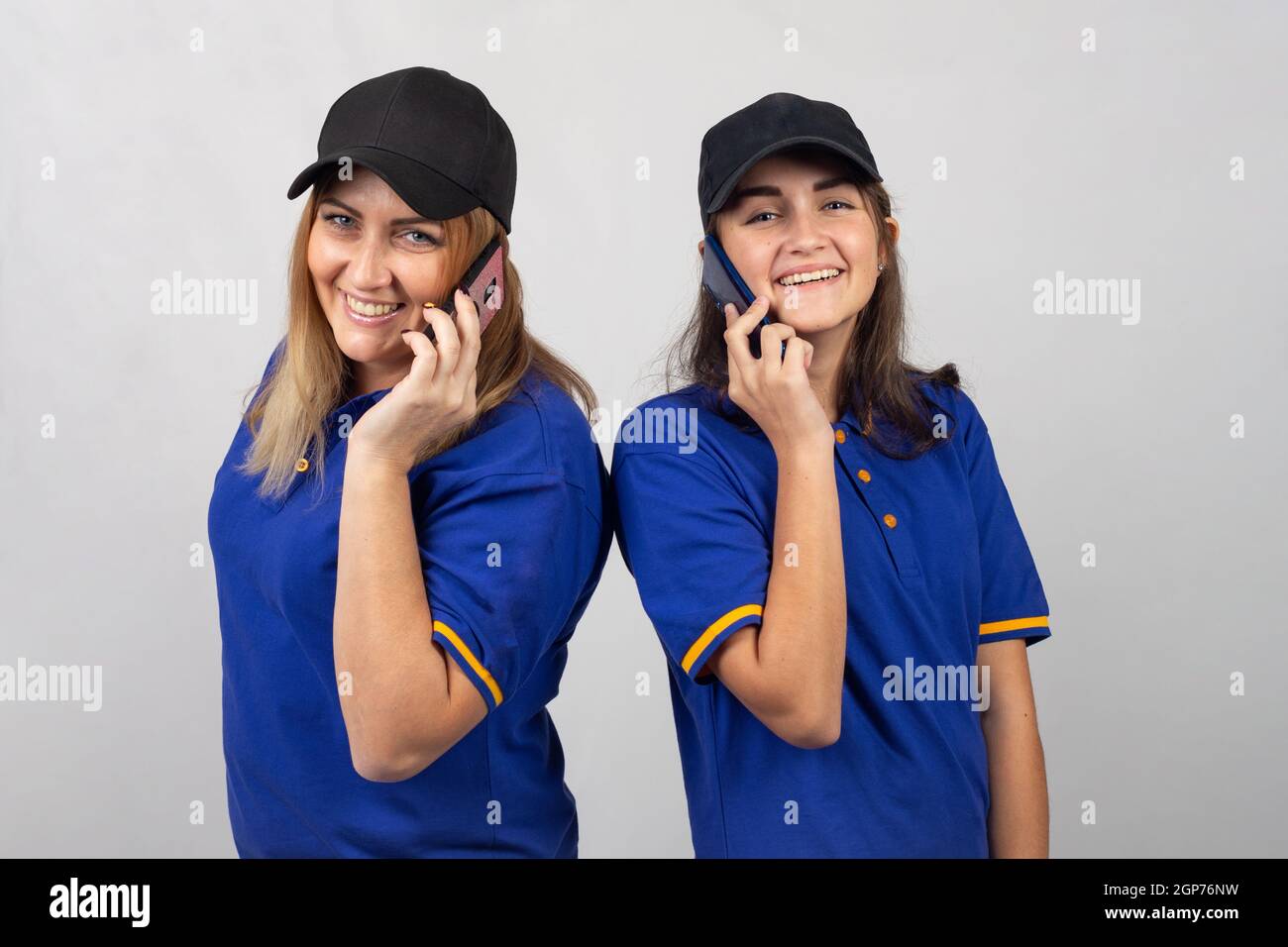 Mother and daughter are standing with their backs to each other, talking on the phone and looking into the frame Stock Photo