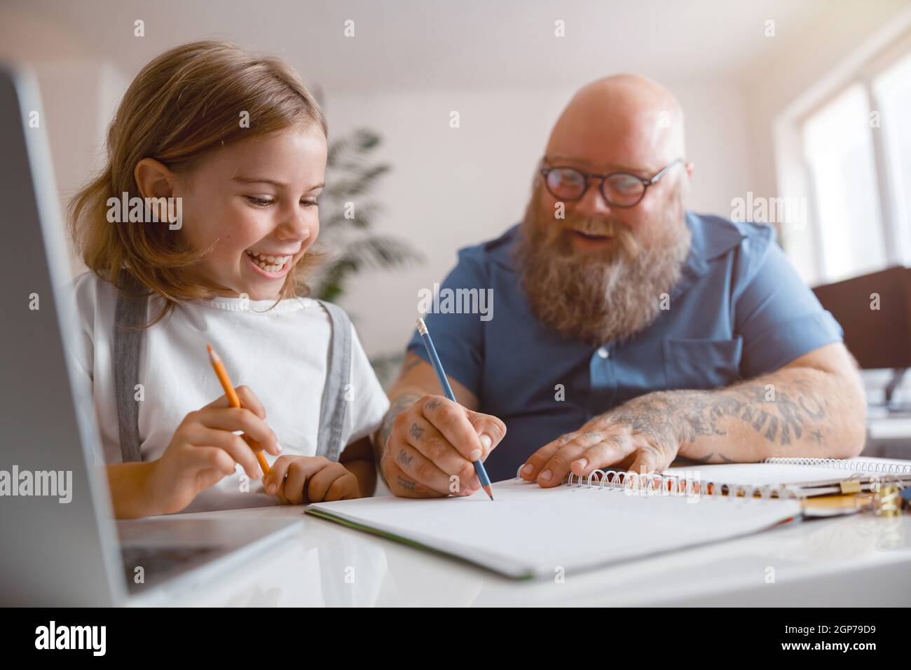 Happy little schoolgirl and father helping her to do homework at table in room Stock Photo