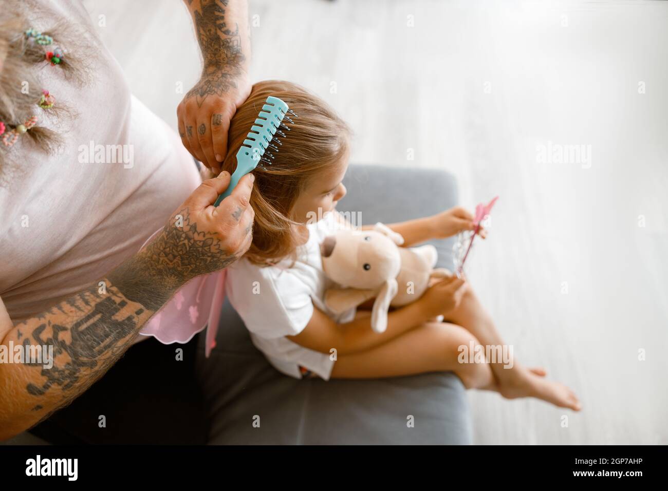 Man with scrunchies in beard brushes girl hair in living room Stock Photo