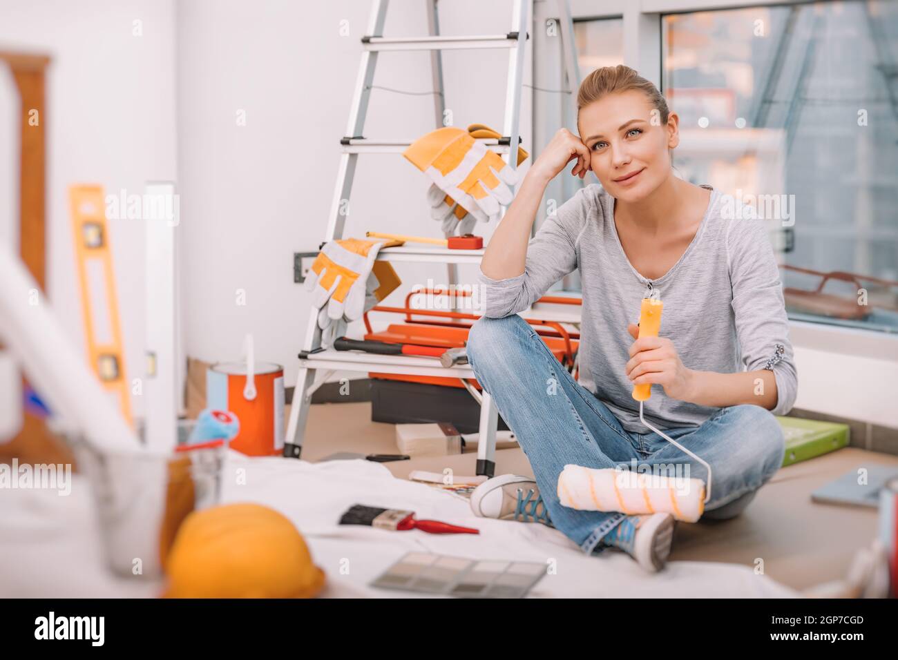Dreamy Girl Sits on the Floor in the Flat with a Paint Roller and Imagines what a Cool Renovation She Will Make. Repairs in the New Apartment. Stock Photo