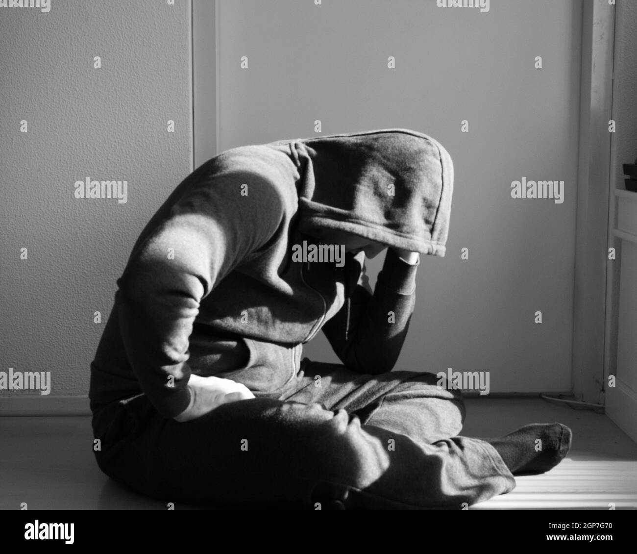 Depressed man sitting on the floor at home in front of a white background wall Stock Photo