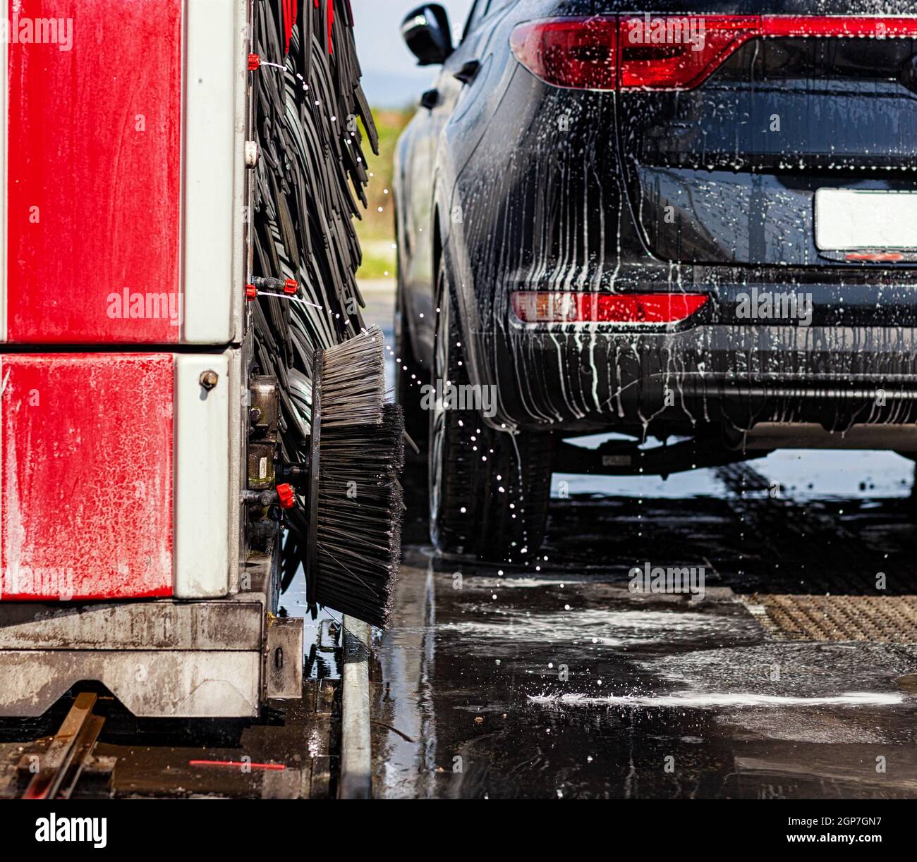 Black car in automatic car wash rotating red and black brush. Detail of