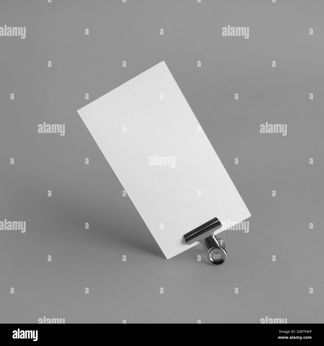 Photo of blank paper business card and binder clip on gray paper background. Mockup for branding identity. Stock Photo