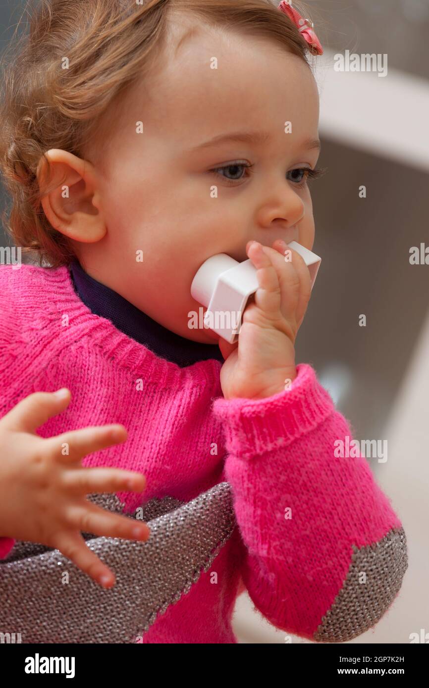 Toddler baby girl plays and puts in her mouth soft rubber building blocks. Stock Photo