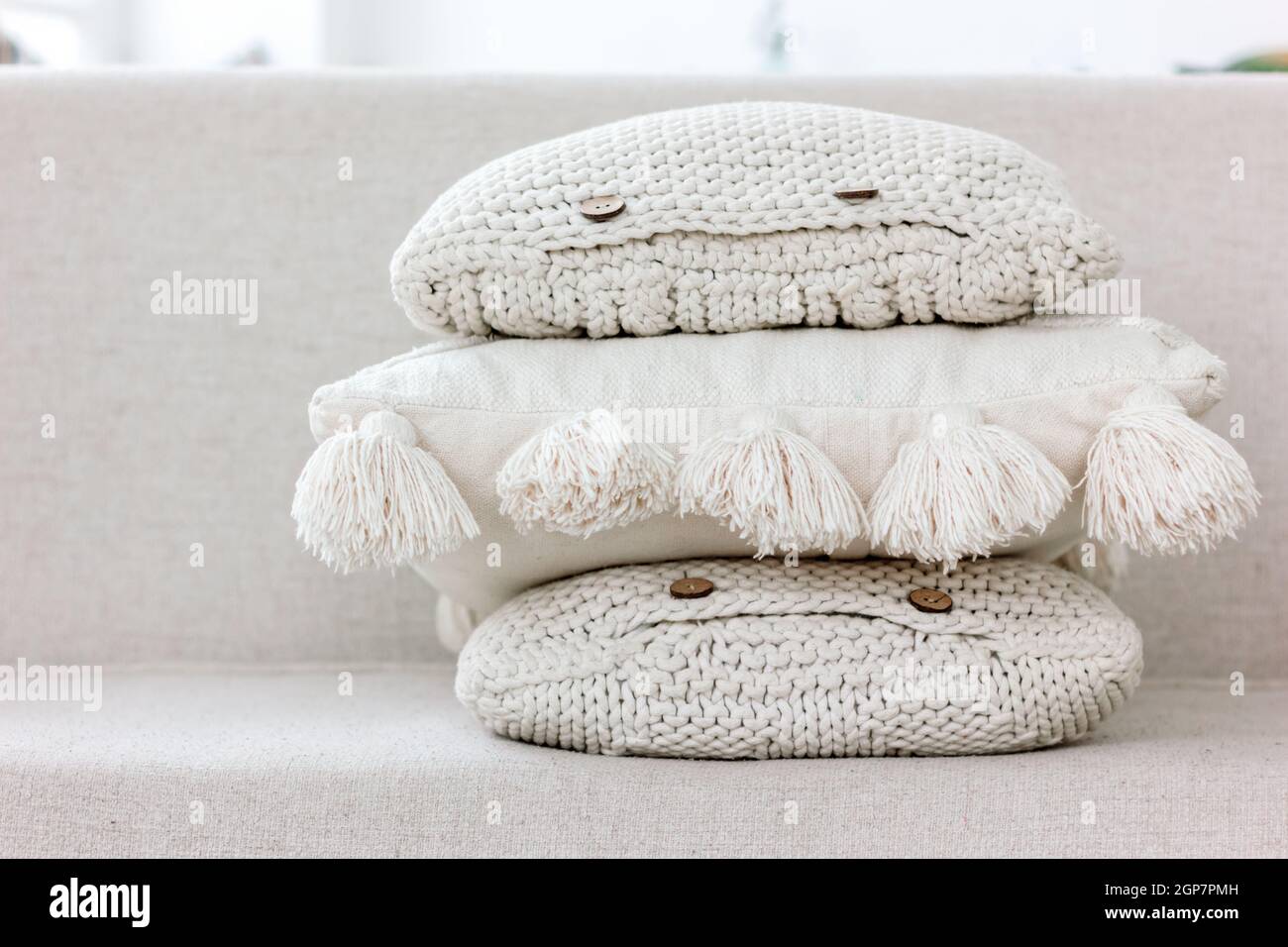A pile of white and beige knitted sofa pillows with buttons and cotton tassels. Cozy textile textures, interior hygge and home handmade design concept Stock Photo