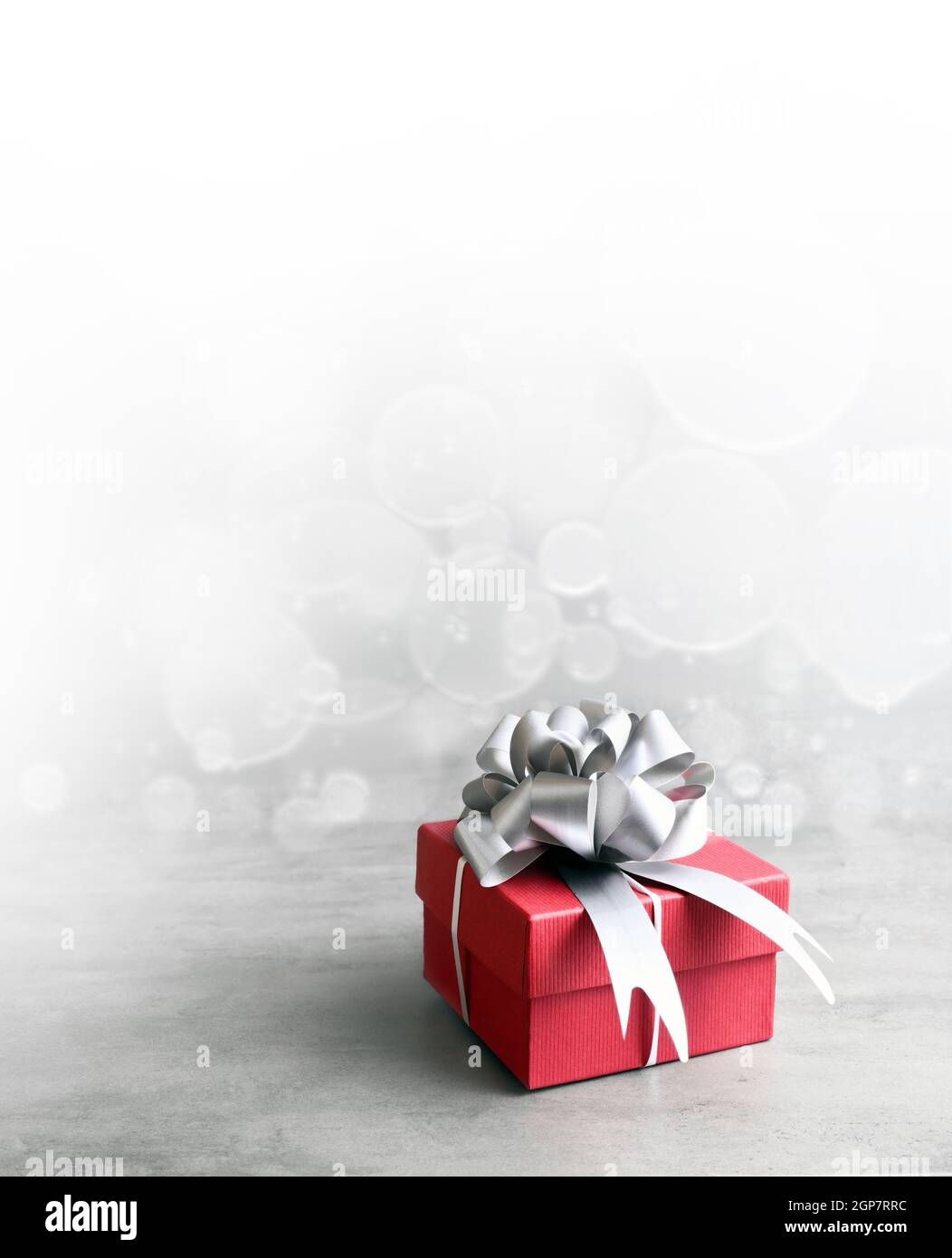 Single red gift box with silver ribbon on grey background. Stock Photo