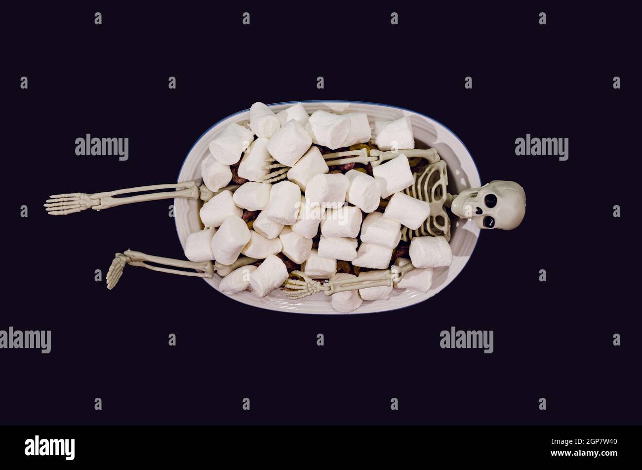 A sceleton taking a bath in a bath tube filled with white marshmallows. Trick or treat Halloween party invitation concept. Funny and spooky artistic d Stock Photo