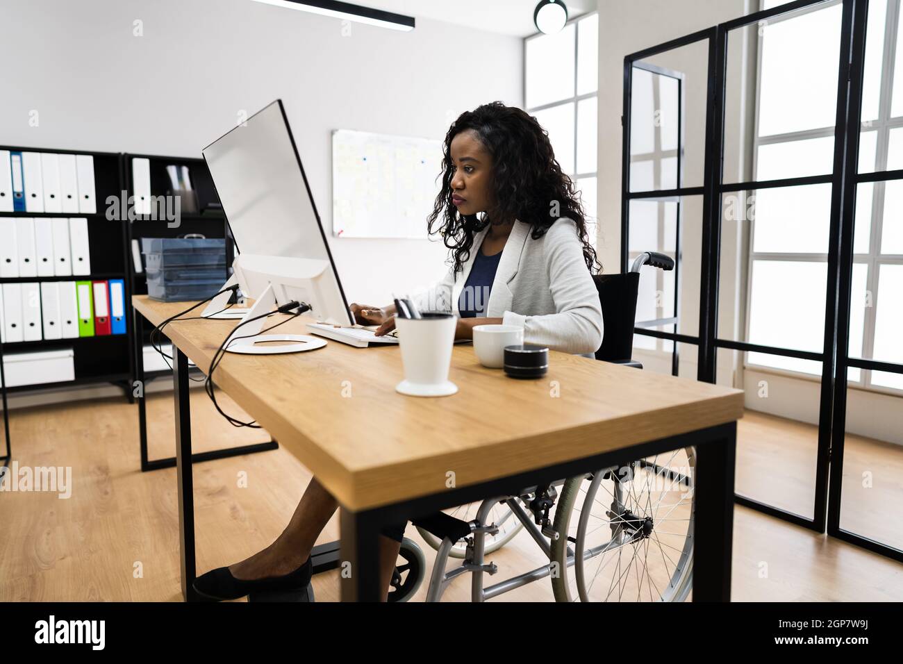 Disabled African Worker In Wheelchair Working On Computer Stock Photo