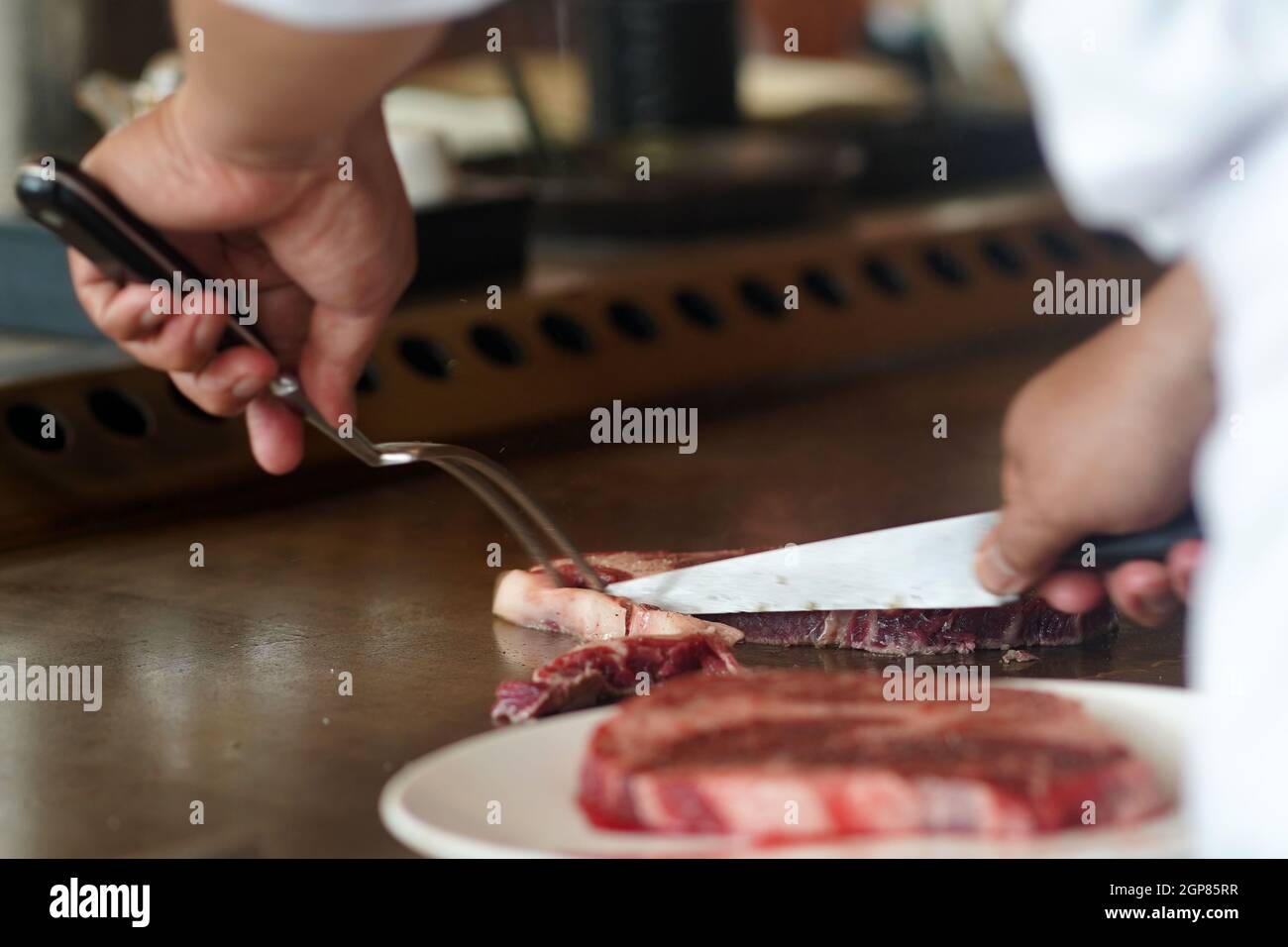 Chef trimming the excess fat from beef meat by a knife on a hot steel ...