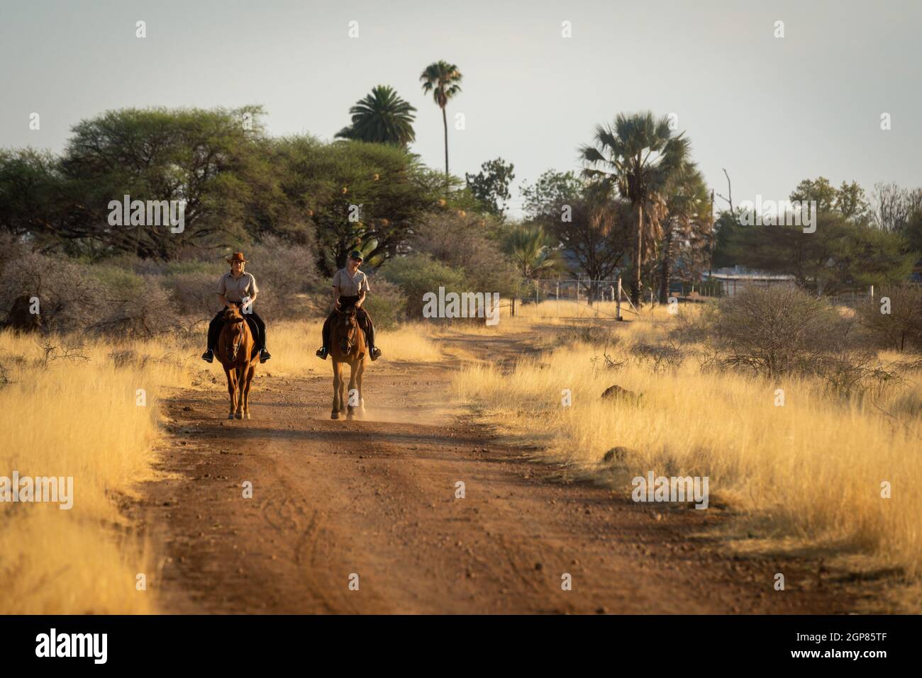 Two horsewomen ride along dirt track side-by-side Stock Photo