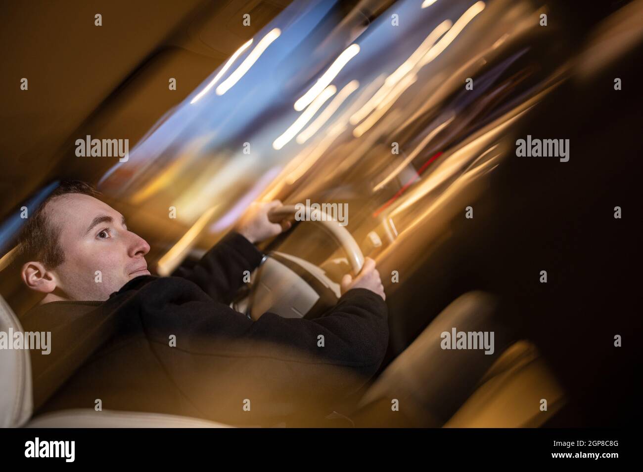 Handsome young man driving his car at night (color toned image; motion ...
