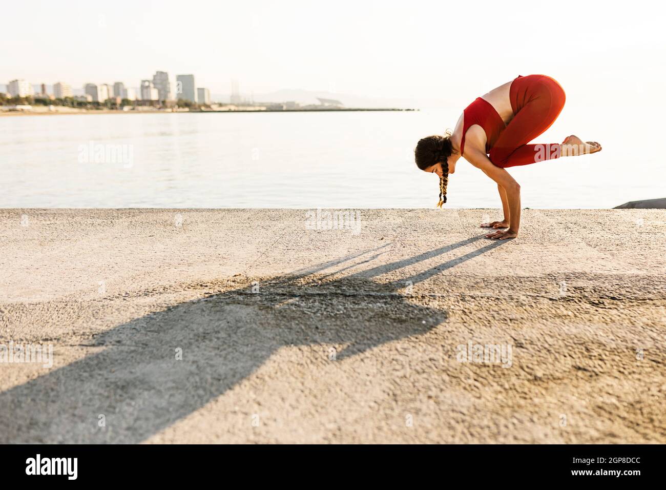 Young hispanic woman practicing yoga and doing bakasana position by the sea Stock Photo