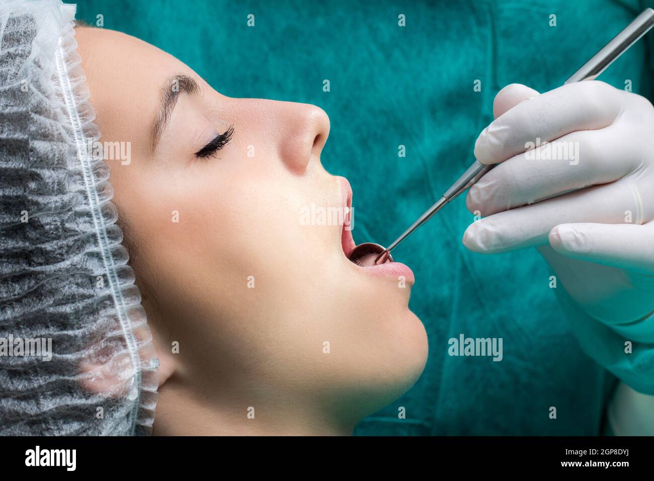 Close up macro side view face shot of woman being prepared for dental surgery.Hand with glove doing check up with mouth mirror on teeth. Stock Photo