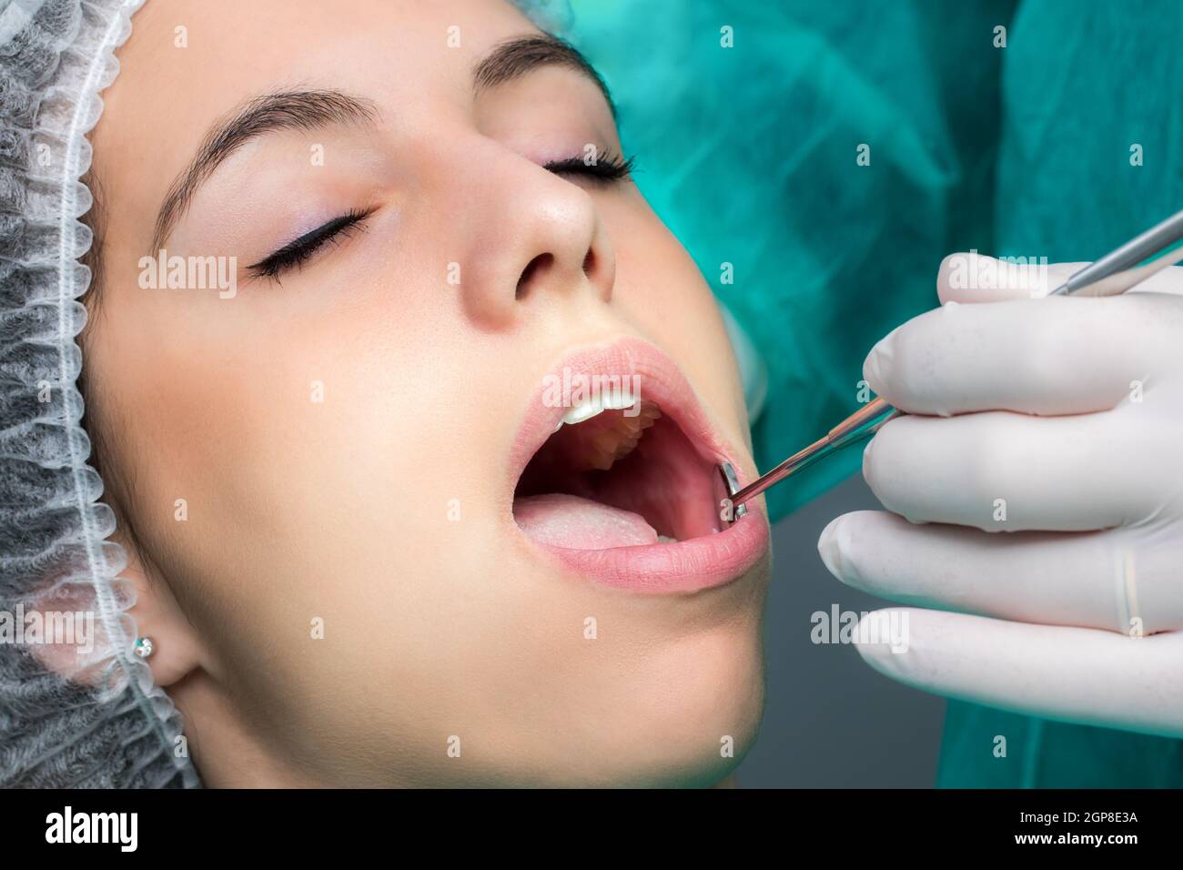 Close up macro face shot of woman being prepared for dental surgery.Hand with glove doing check up with mouth mirror on teeth. Stock Photo