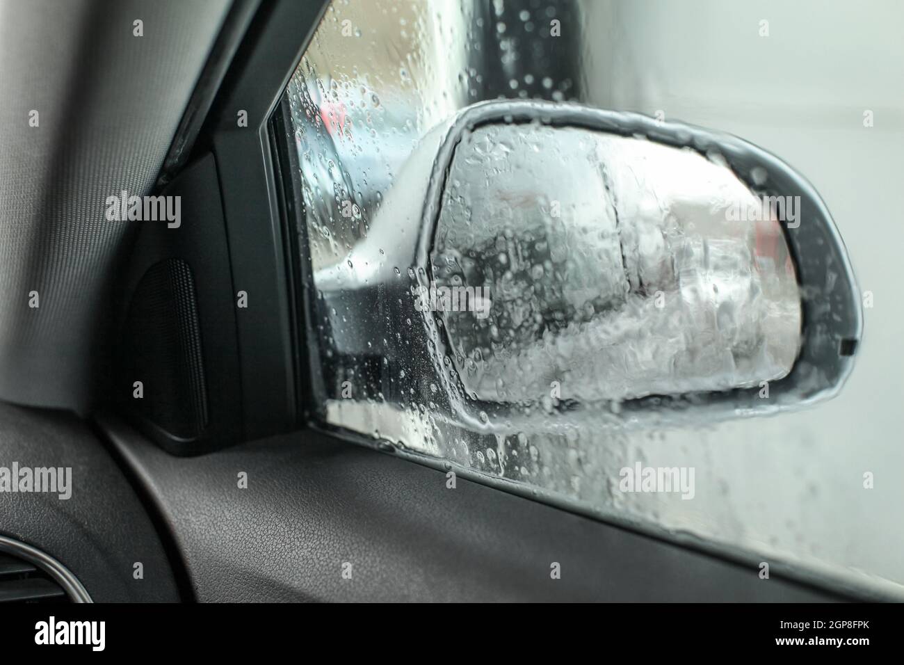 View from inside the car, looking at side mirror, wet from water and soap when being washed in carwash. Stock Photo