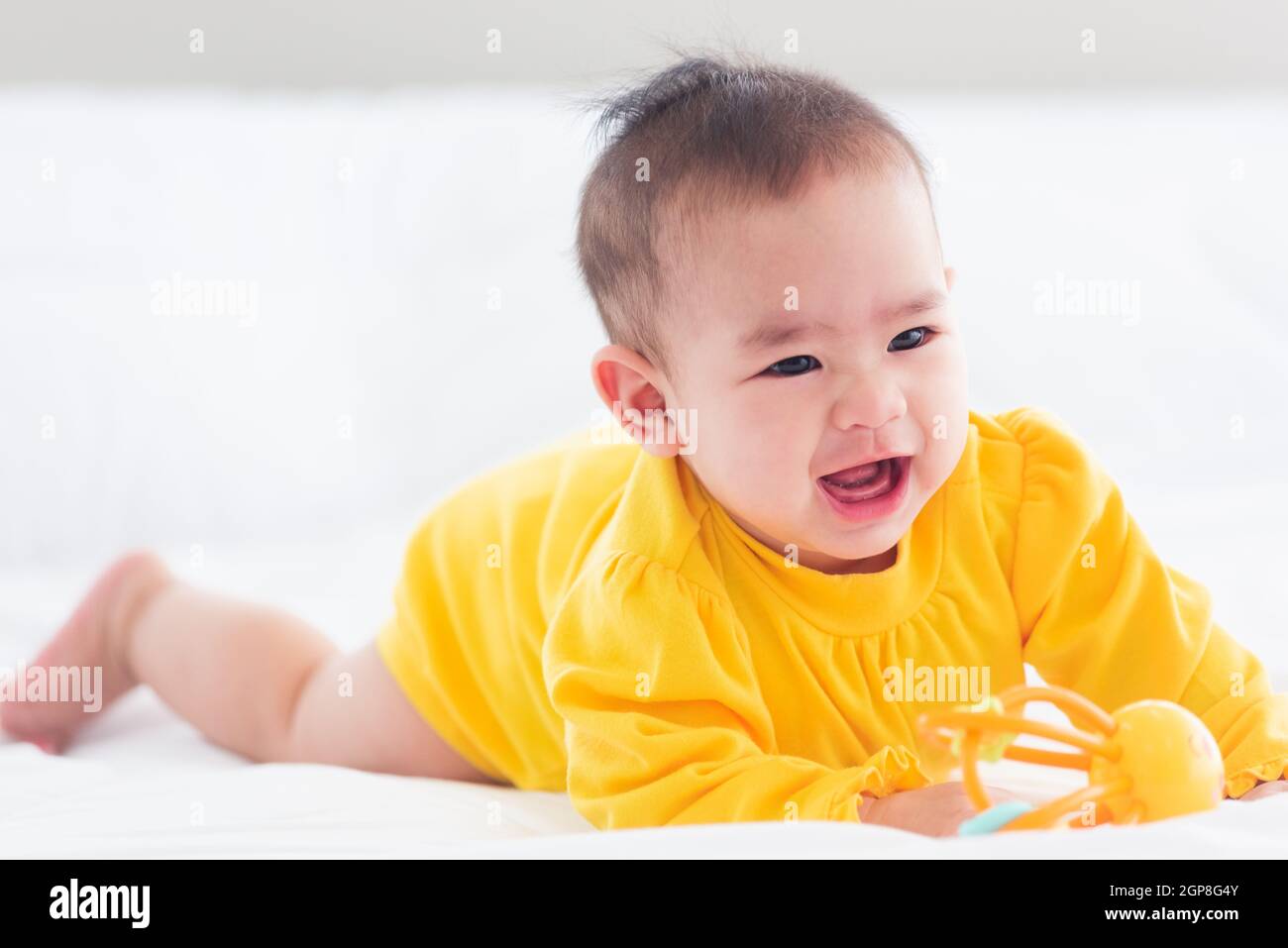 Portrait of beautiful young Asian newborn little baby prone on the bed at home, Happy baby smile wears a yellow shirt relaxing in the room, Family mor Stock Photo