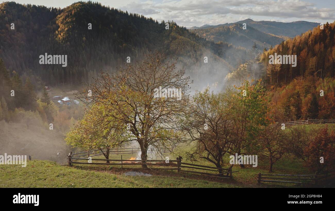 Aerial of haze clouds over mountain village. Fields, grass valley, forest at cottages in smoky fog. Autumn nobody nature landscape. Wild fire concept. Countryside Carpathian mounts, Ukraine, Europe Stock Photo