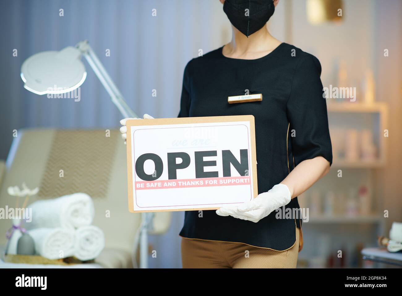 Business during covid-19 pandemic. Closeup on woman worker with ffp2 mask and open sign in modern beauty studio. Stock Photo