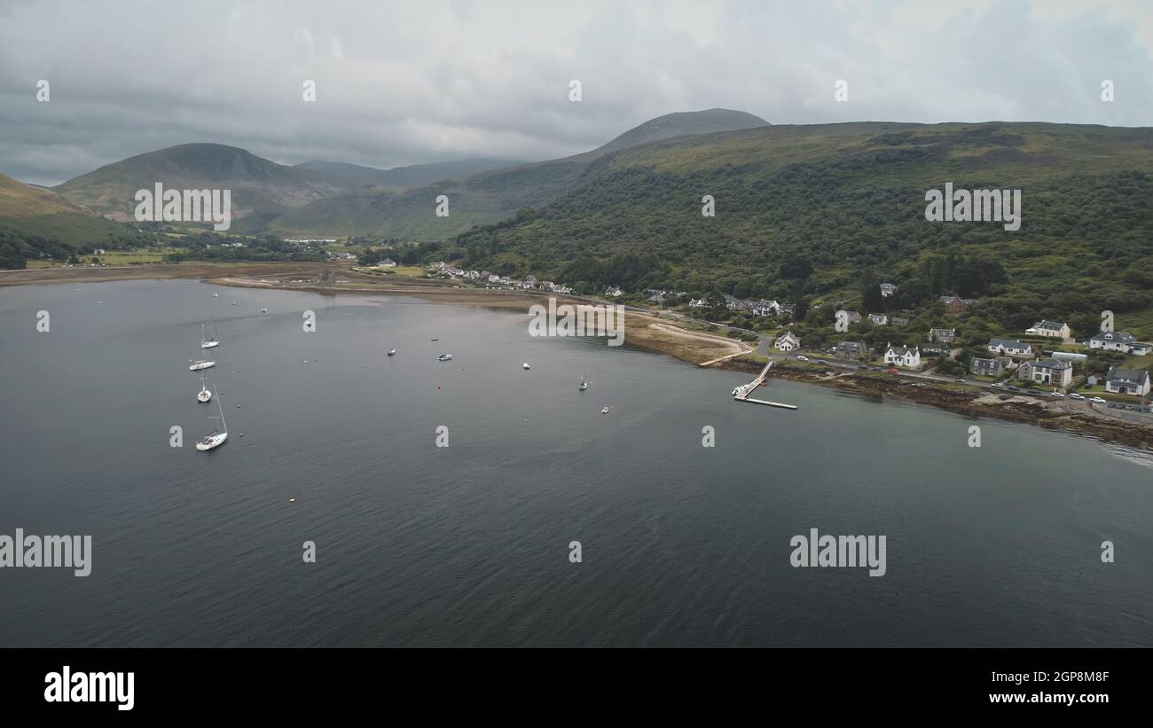 Yachts, ships at green mountain on ocean bay coast aerial. Nobody nature with serene seascape. Water transport at harbor of Arran Island, Scotland. Marine vacation at summer. Cinematic travel, tourism Stock Photo