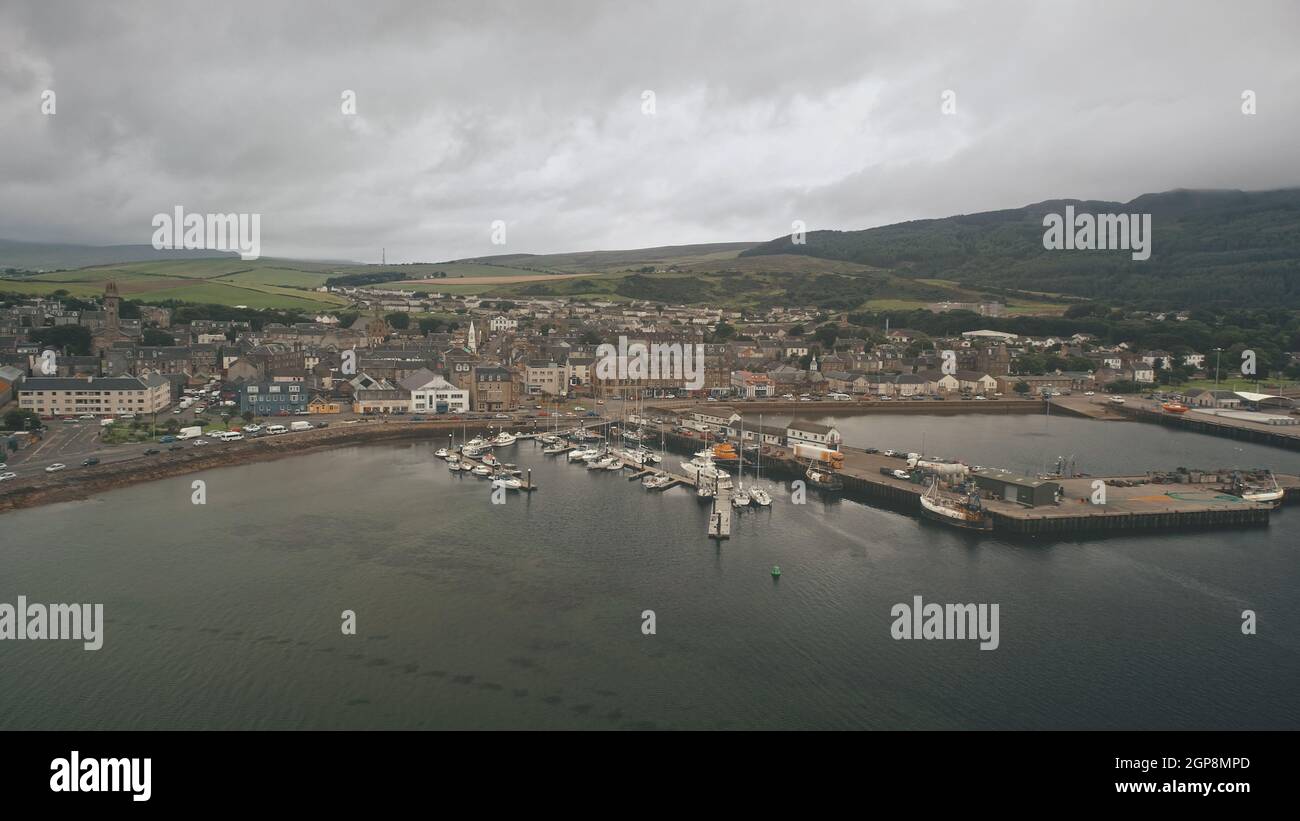 Ships, yachts at sea bay aerial. Cityscape with ancient architecture landmark at ocean pier town Campbeltown, Scotland, Europe. Dramatic streets: old buildings at highway with driving cars at dusk day Stock Photo