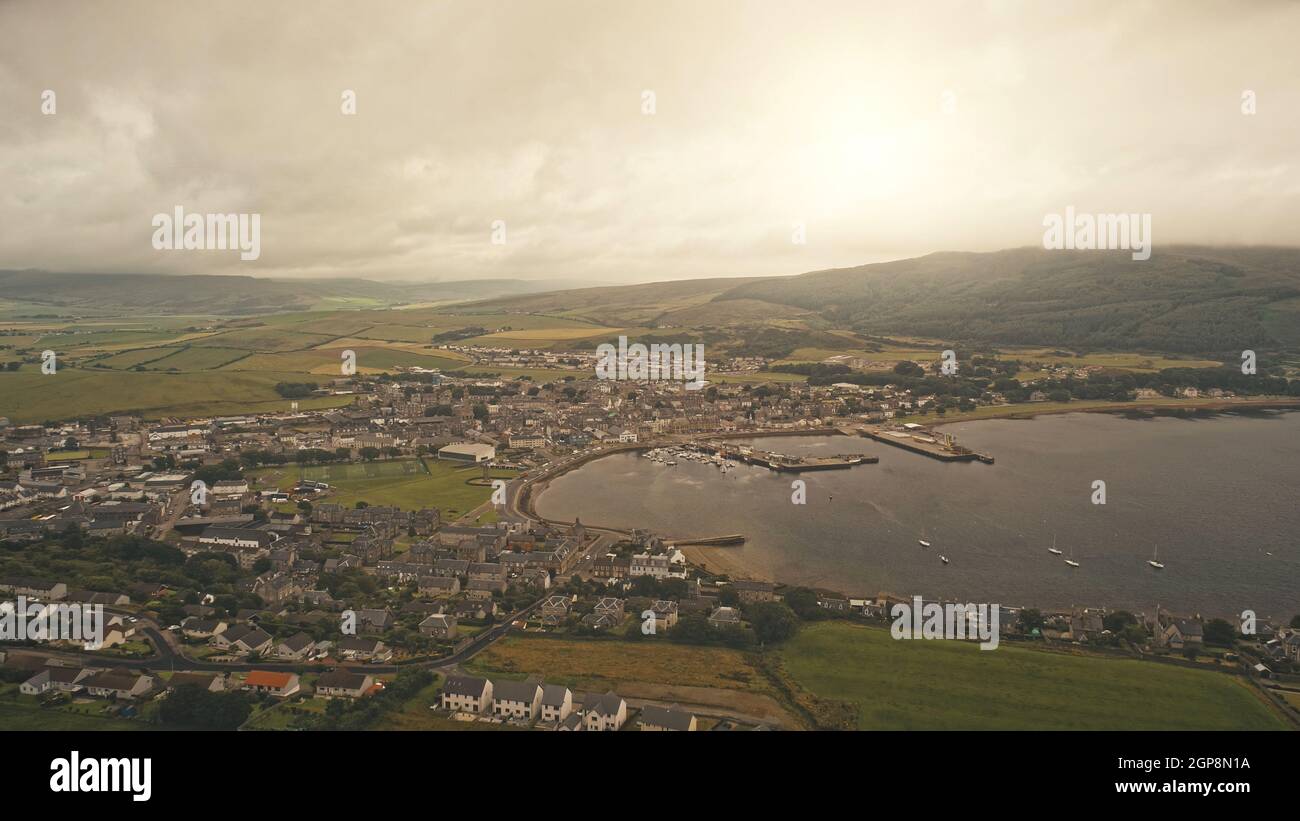 Sun cityscape of port town at sea bay aerial. Traffic highway with driving cars at ocean shore. Modern buildings at Campbeltown city, Scotland, Europe. Boats, yachts at pier. Sunny nature landscape Stock Photo