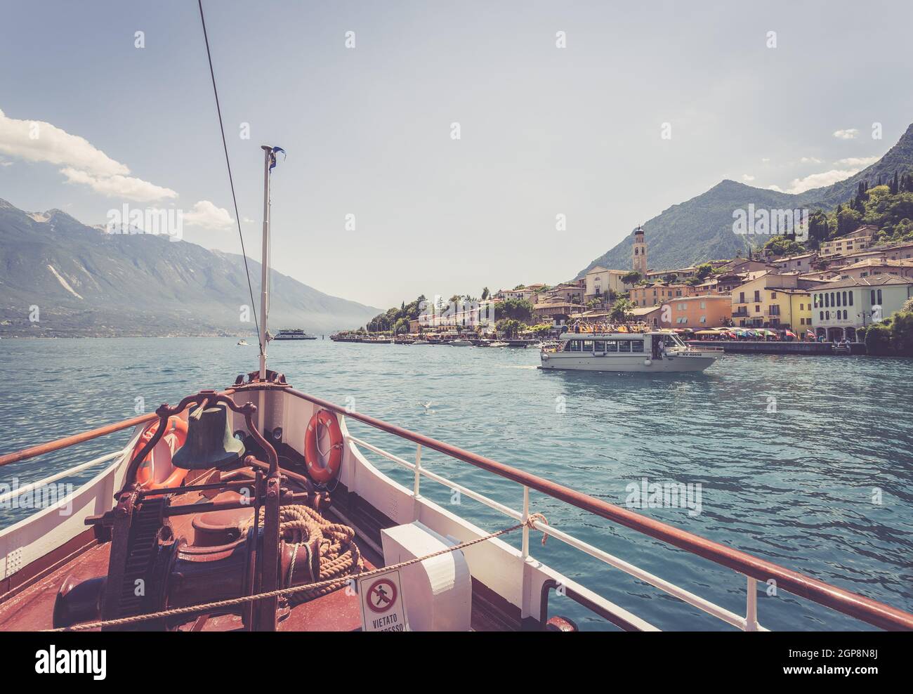 Bow of a boat on a boat tour. Blue water, moutnain range and little village, Lago di Garda, Italy Stock Photo