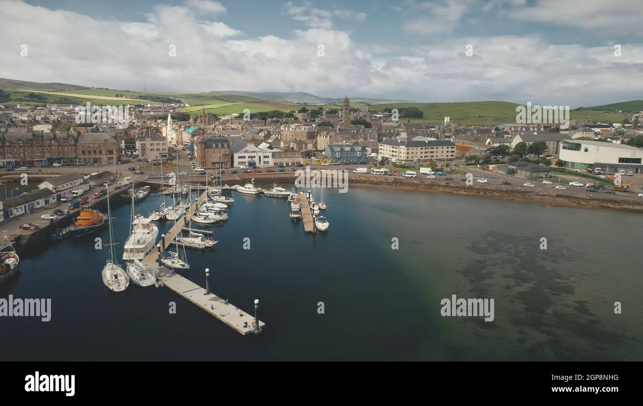 Traffic road at sea bay coast aerial. Pier town with old buildings. Ships and yachts at wharf. Marina seascape at urban highway with cars, vans, trucks. Campbeltown cityscape, Scotland, Europe Stock Photo