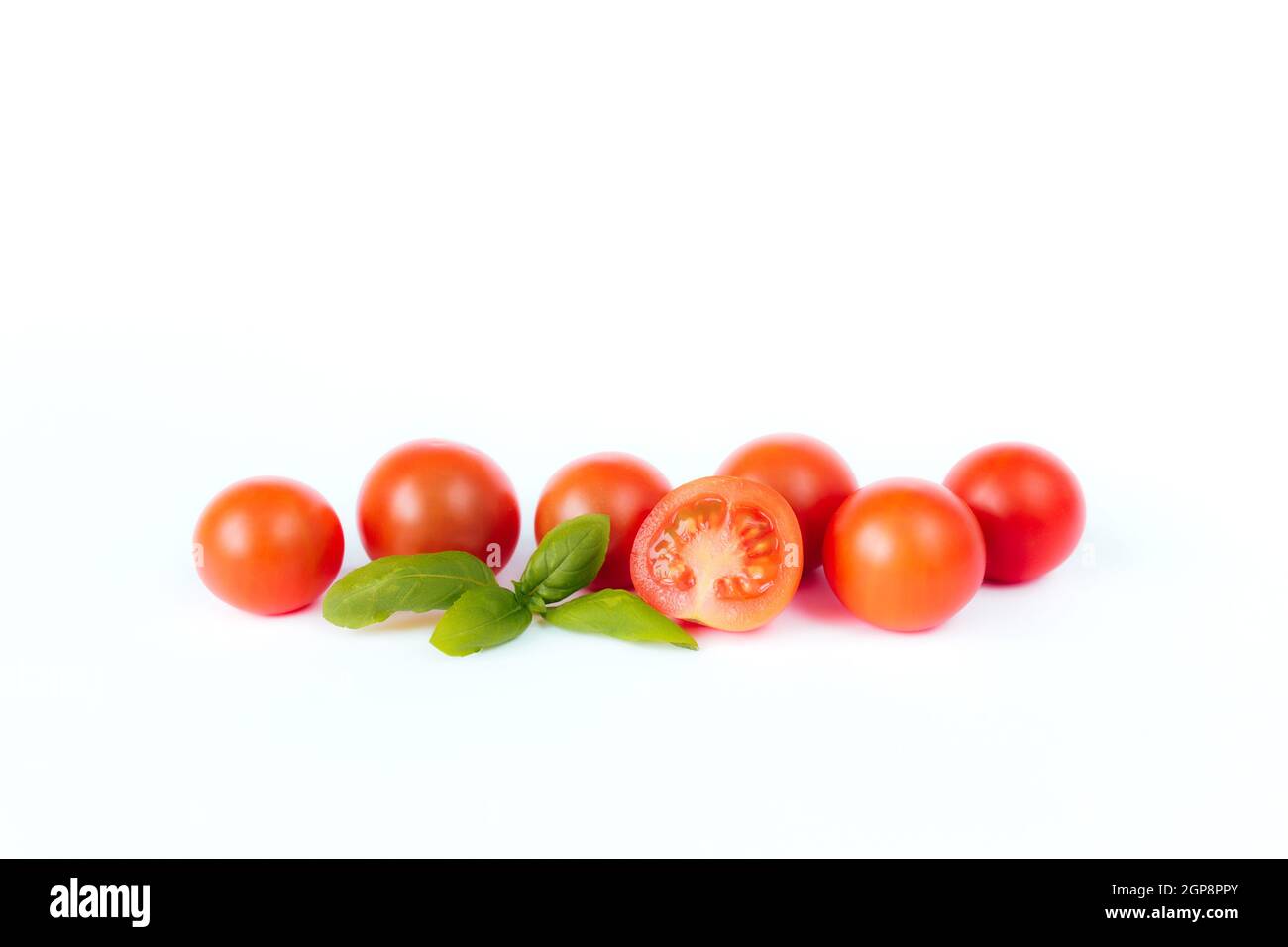 Red cherry tomatoes with green basil on a white background. High quality photo Stock Photo