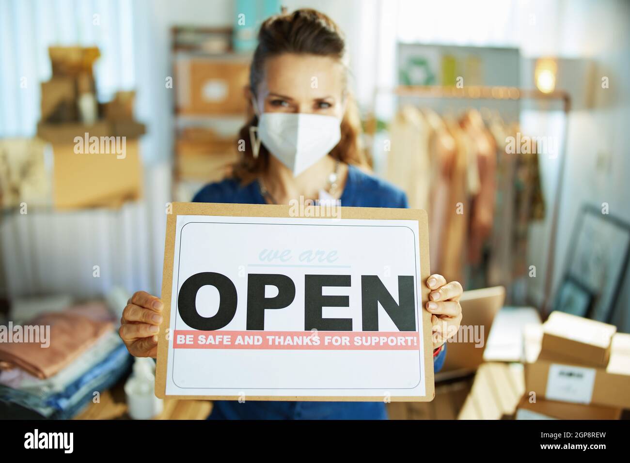 Closeup on small business owner woman with ffp2 mask and open after covid sign in the office. Stock Photo