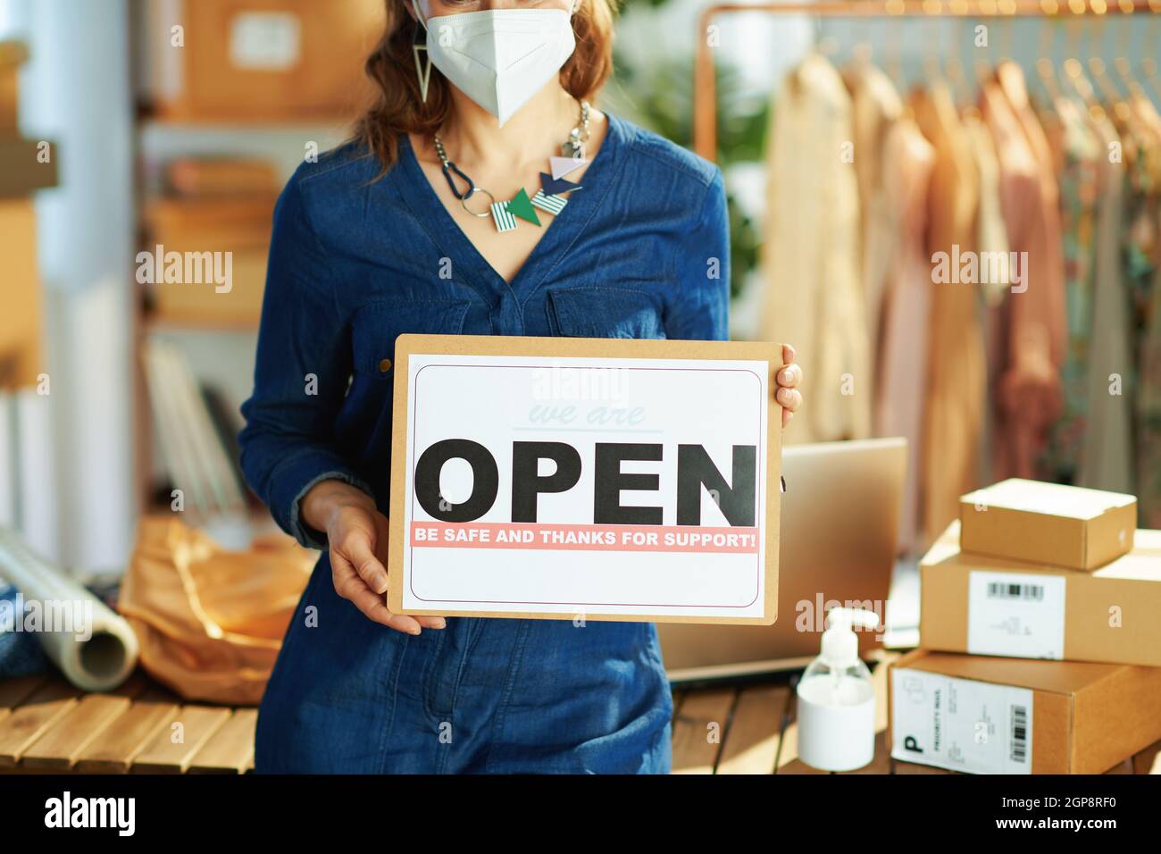 Closeup on small business owner woman with ffp2 mask, parcel, open after covid sign and antiseptic in the office. Stock Photo