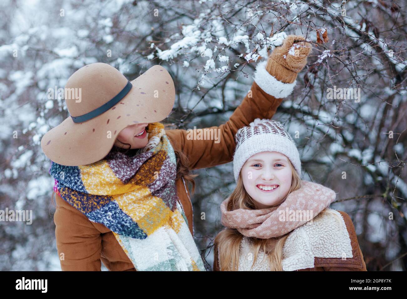 happy elegant mother and child in hats and sheepskin coats with mittens playing outdoors in the city park in winter. Stock Photo