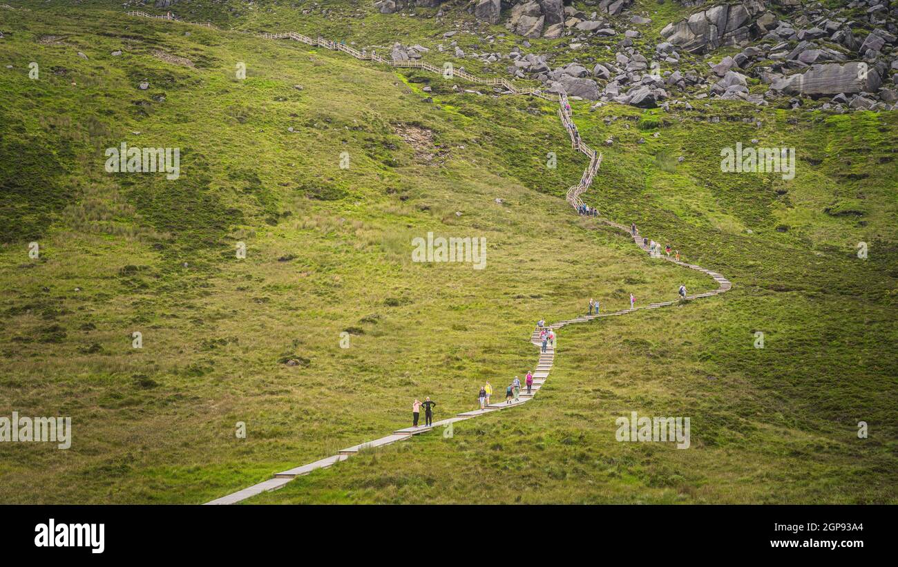 People hiking on wooden boardwalk, climbing on steps and stairs to Cuilcagh Mountain. Steep mountainside with boulders and rubble, Northern Ireland Stock Photo